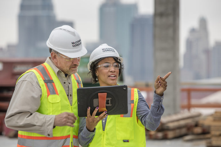 Two employees in hardhats on site pointing at the project